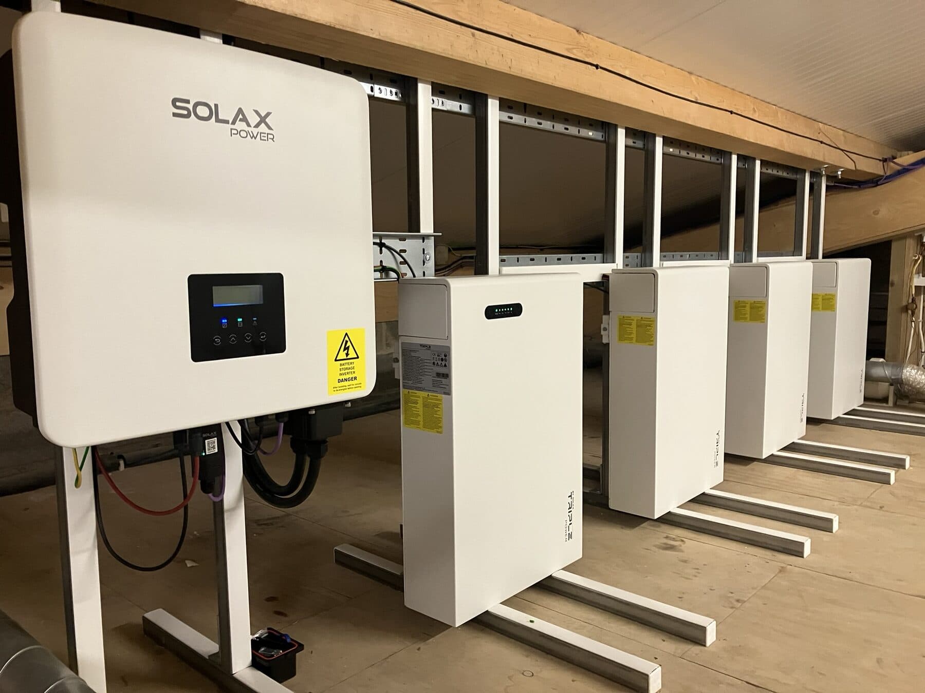 Solax inverter wired to a bank of four home battery storage units mounted on a plant room wall
