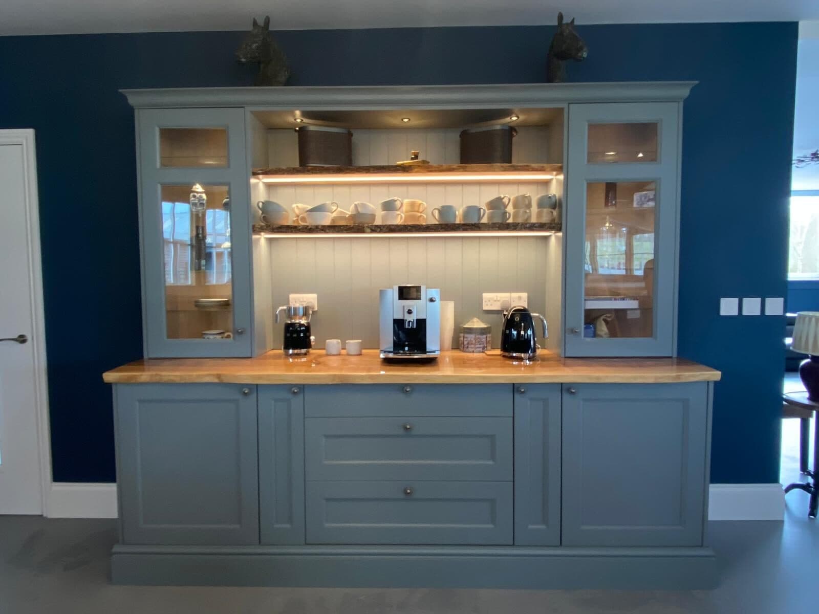 Painted kitchen dresser against a deep blue wall with LED lighting under the shelf and sockets set into the cabinet sides