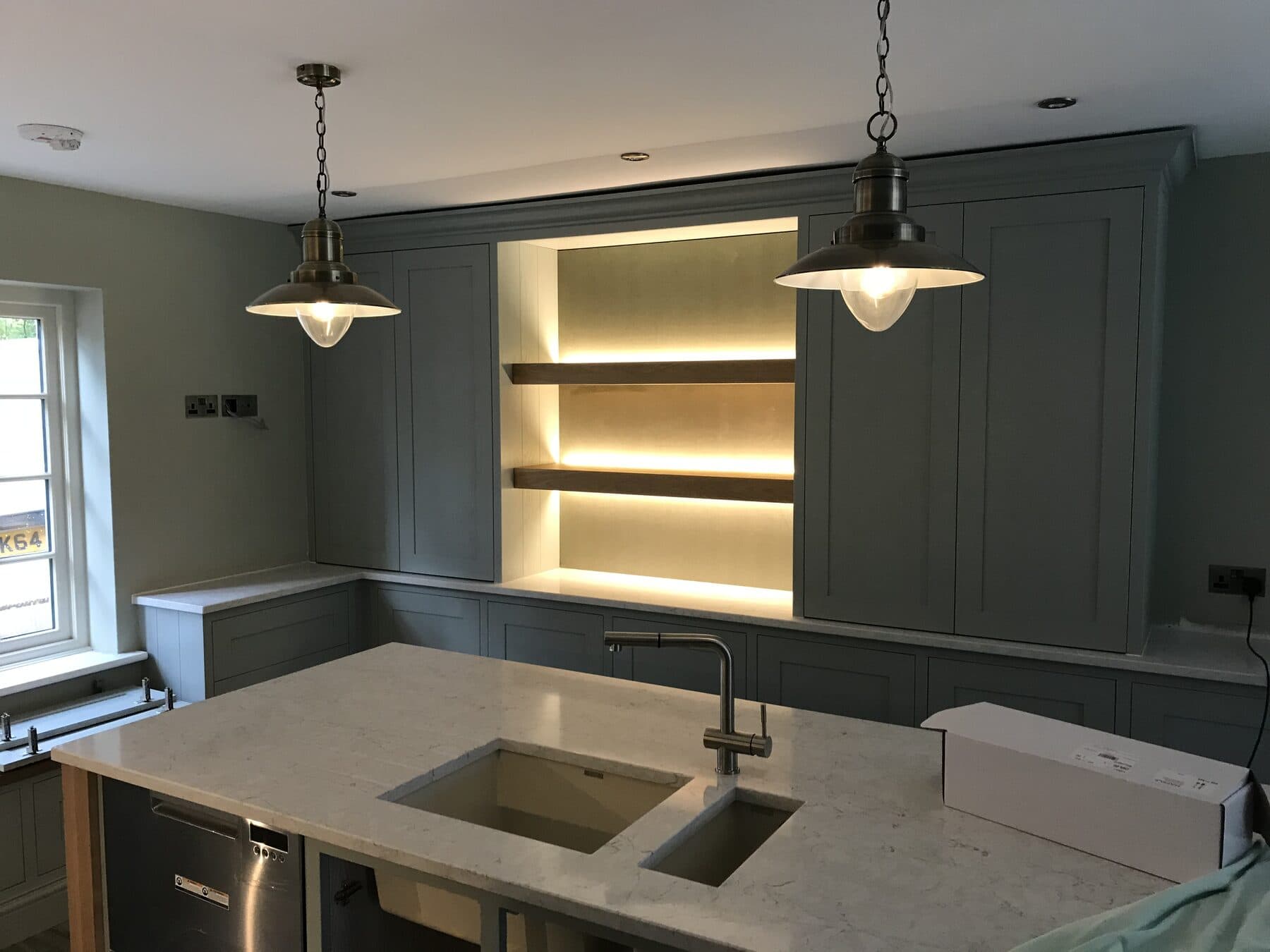 Shaker kitchen in a Cheltenham home with glass pendant lights over the island and warm LED strip lighting behind open oak shelves